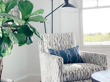White and black swivel chair next to window with blue rug and pillow and modern black lamp.