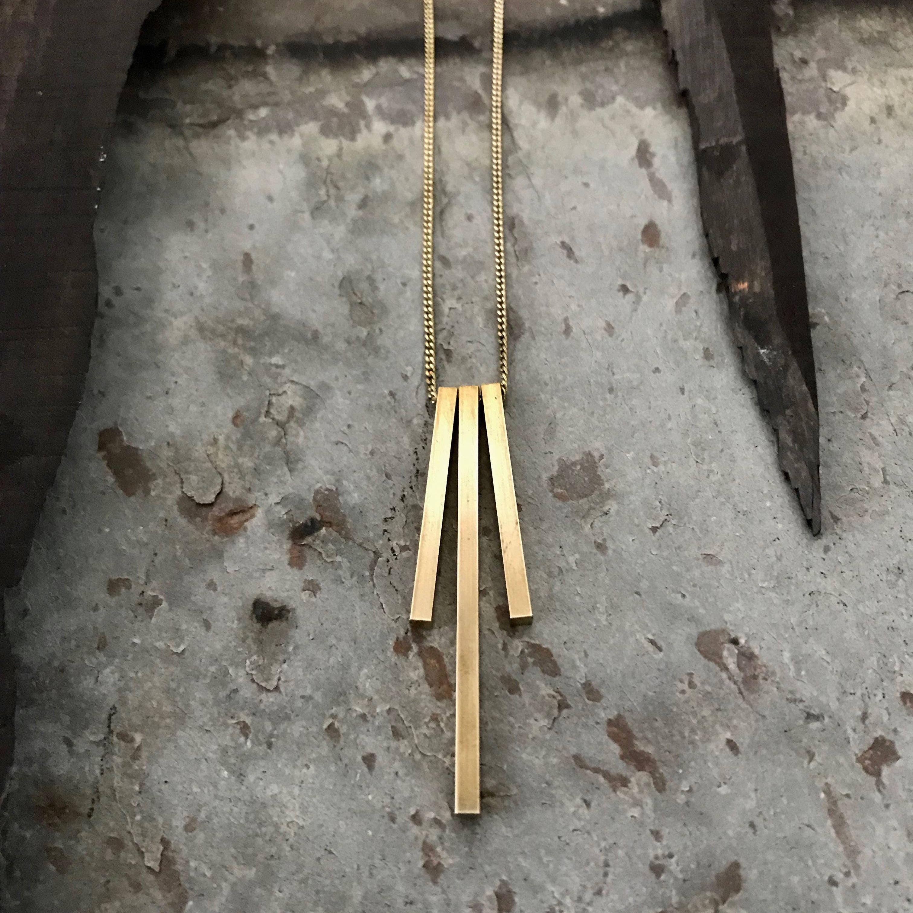 Tiny Anvil Brass Tri Pillar Necklace on a grey background at Addison West