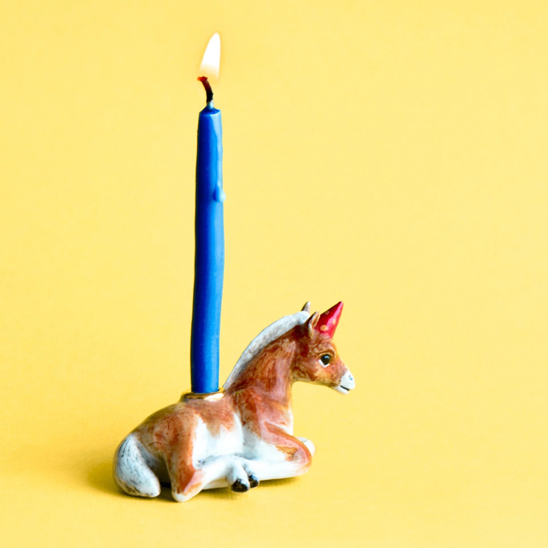 horse-shaped candle holder with a red hat and a blue candle on a yellow background