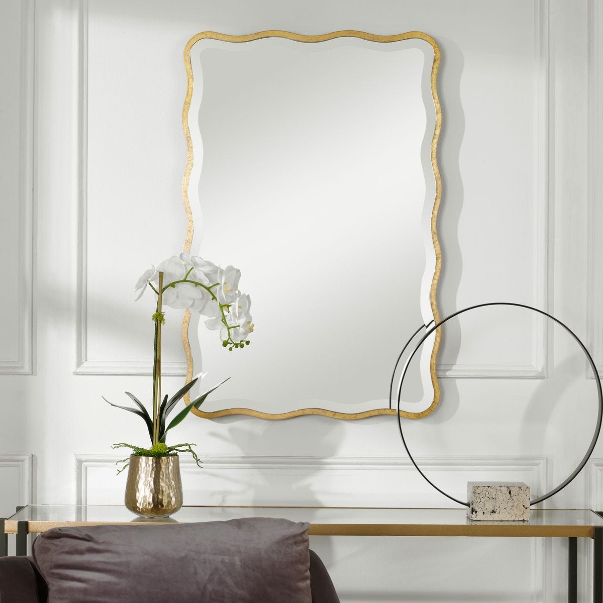 Anesley Accent Mirror in Gold on a white wall above a table at Addison West