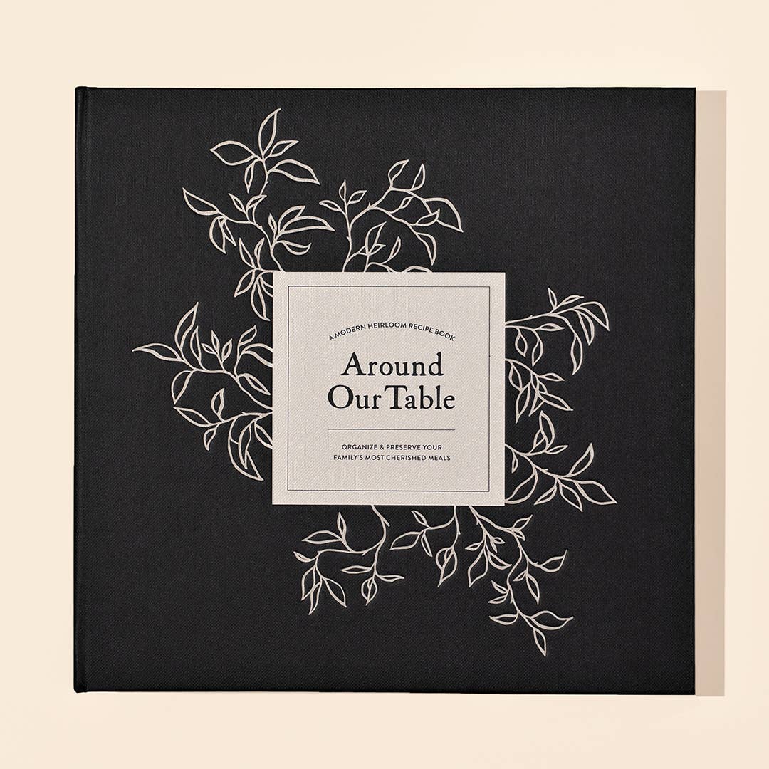 Black book titled 'Around Our Table' with white leaf designs on a beige background