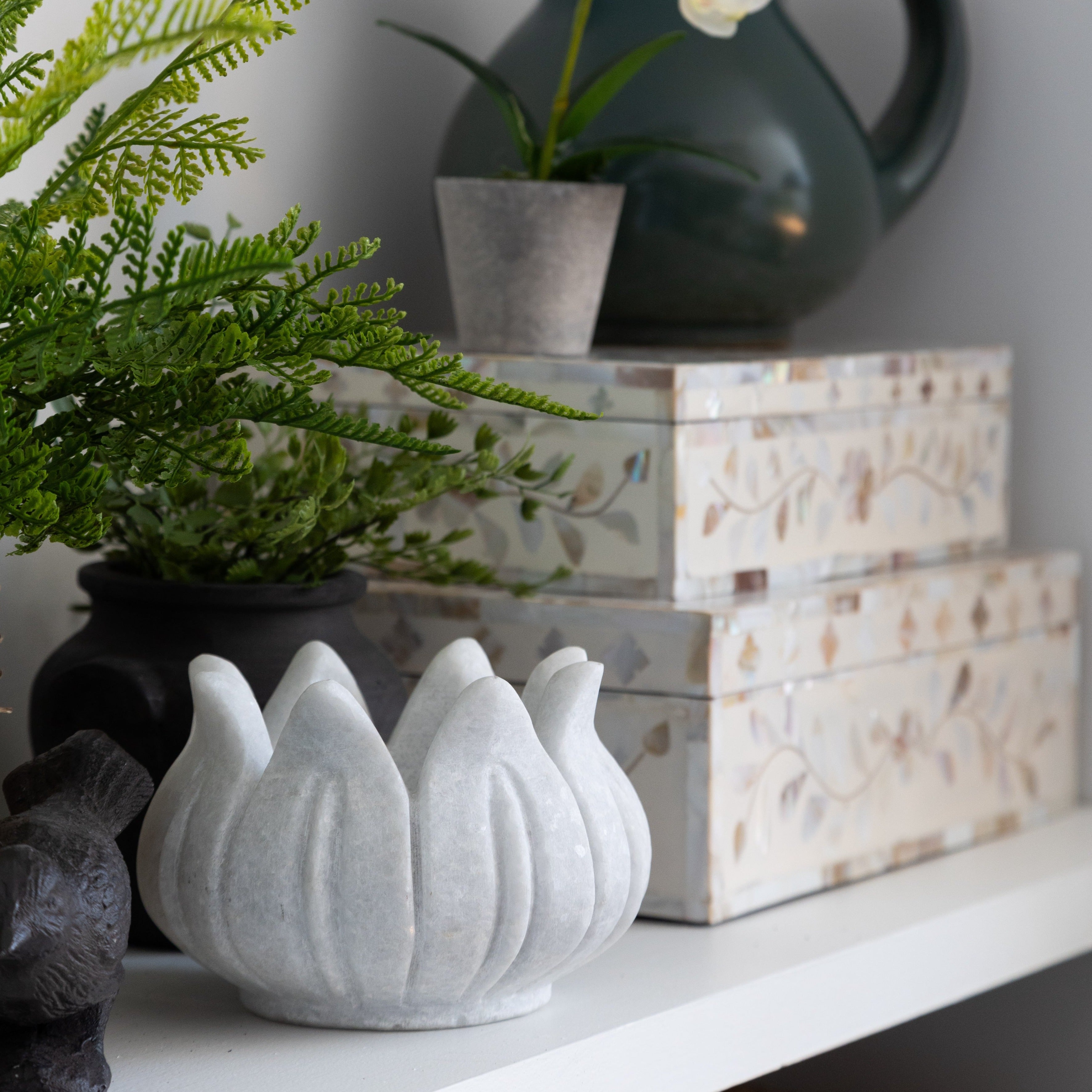 White marble lotus bowl on a shelf near decorative boxes and other items