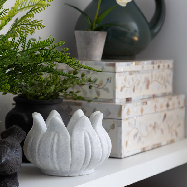 White marble lotus bowl on a shelf near decorative boxes and other items 
