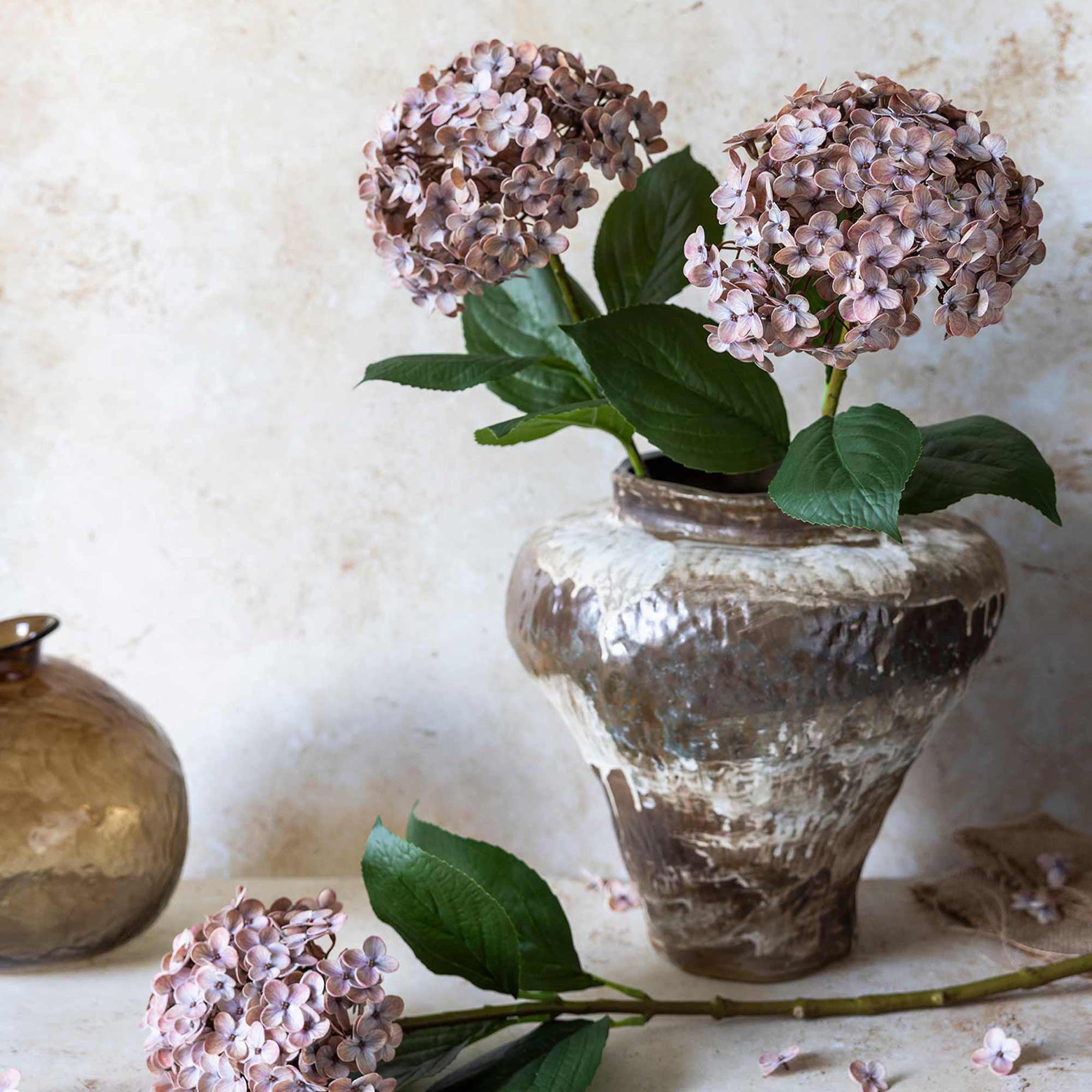 Decorative vase with pink flowers and green leaves on a textured surface
