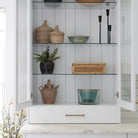 White kitchen cabinet with glass doors open to shelves decorated with wood bowls and kitchen accessories