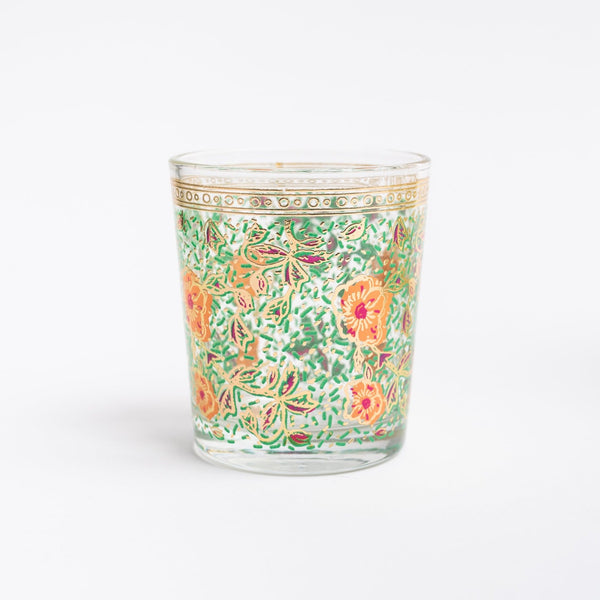 Drinking glass with green and organge floral pattern on a white wood surface