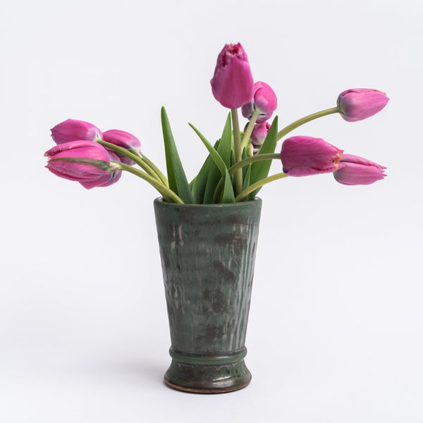 Aged olive dripped glaze vase with flowers in it on a white background 