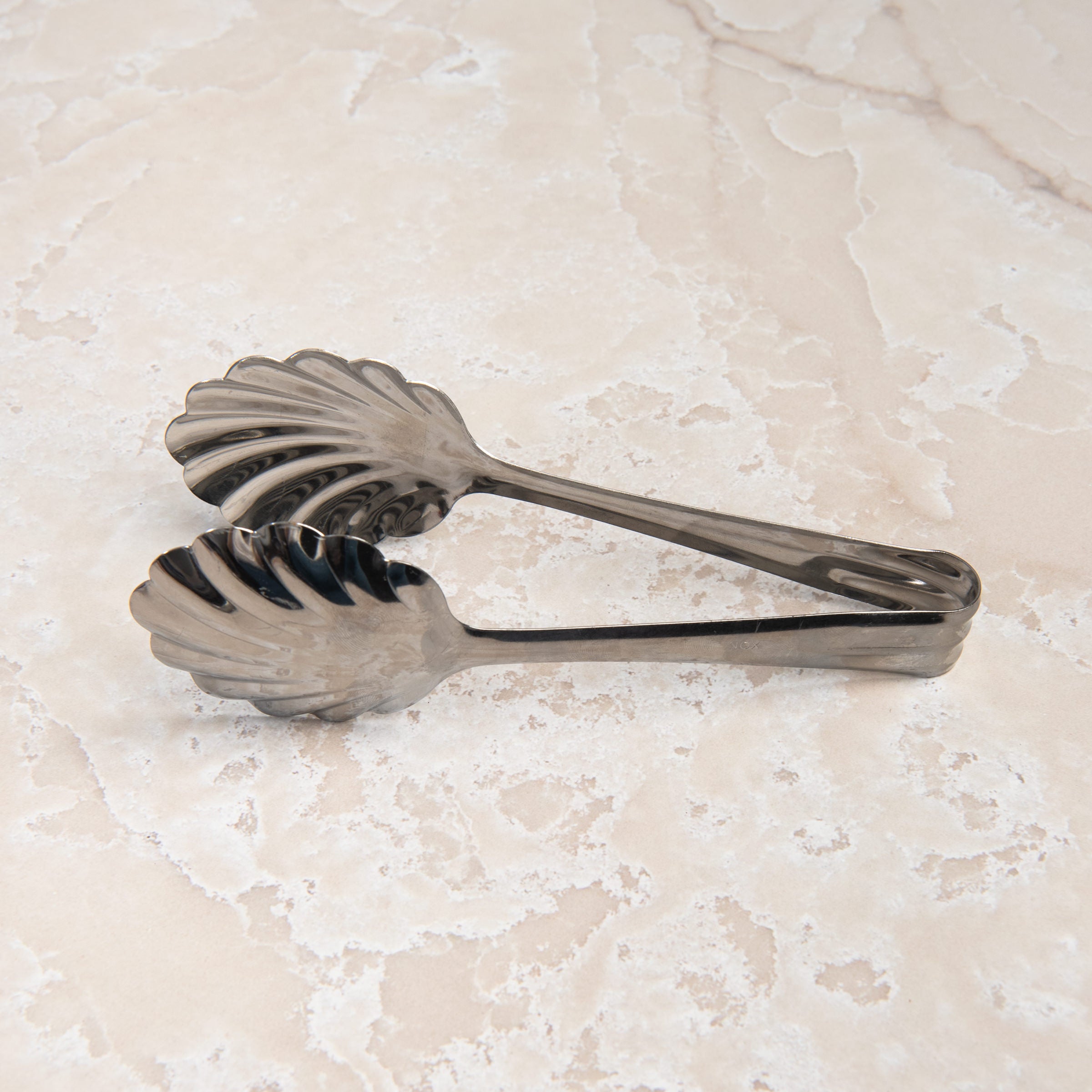 Scalloped Serving Tongs on a beige background at Addison West