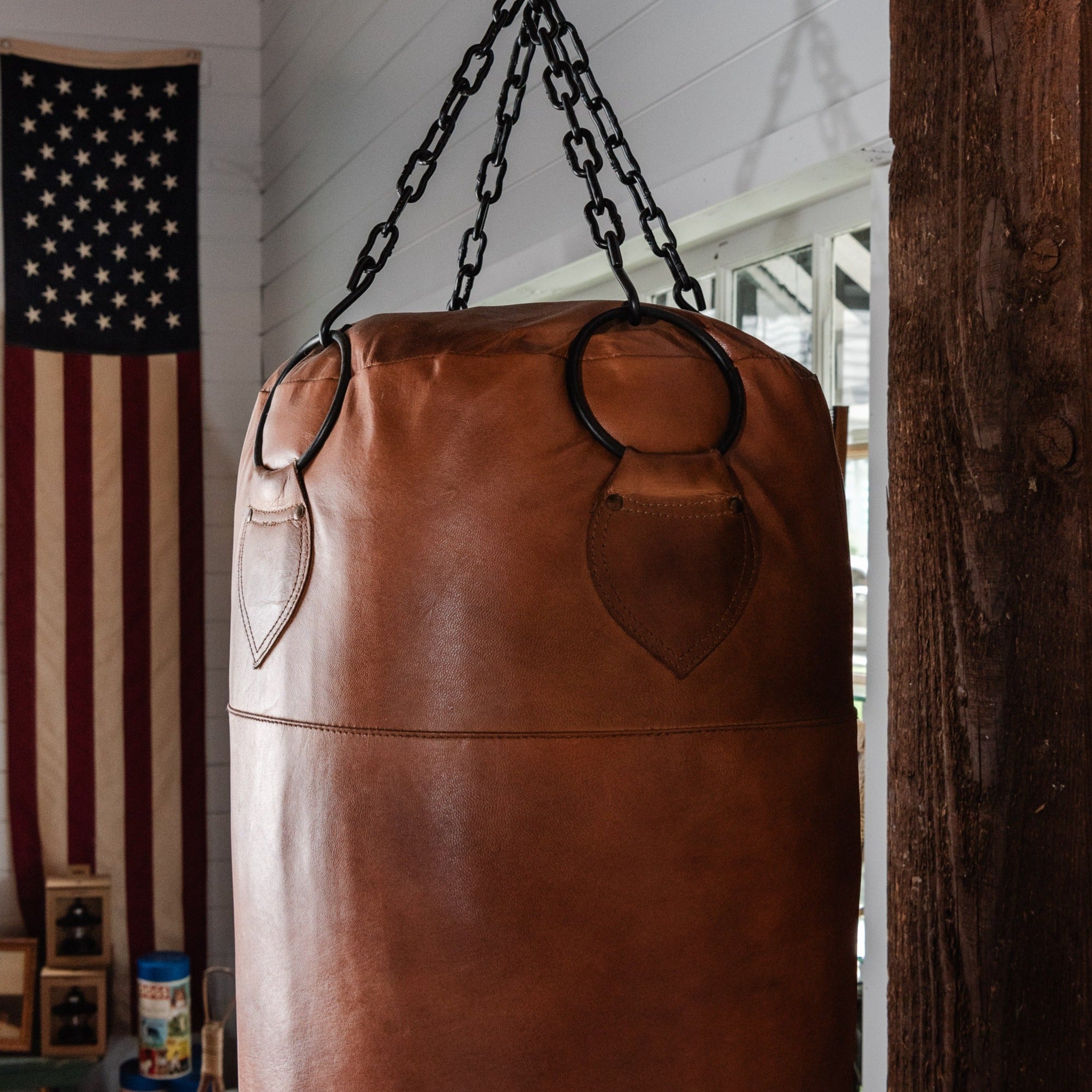 Pugilist Bag vintage punching bag in a room with ship lap walls and an American flag in the background