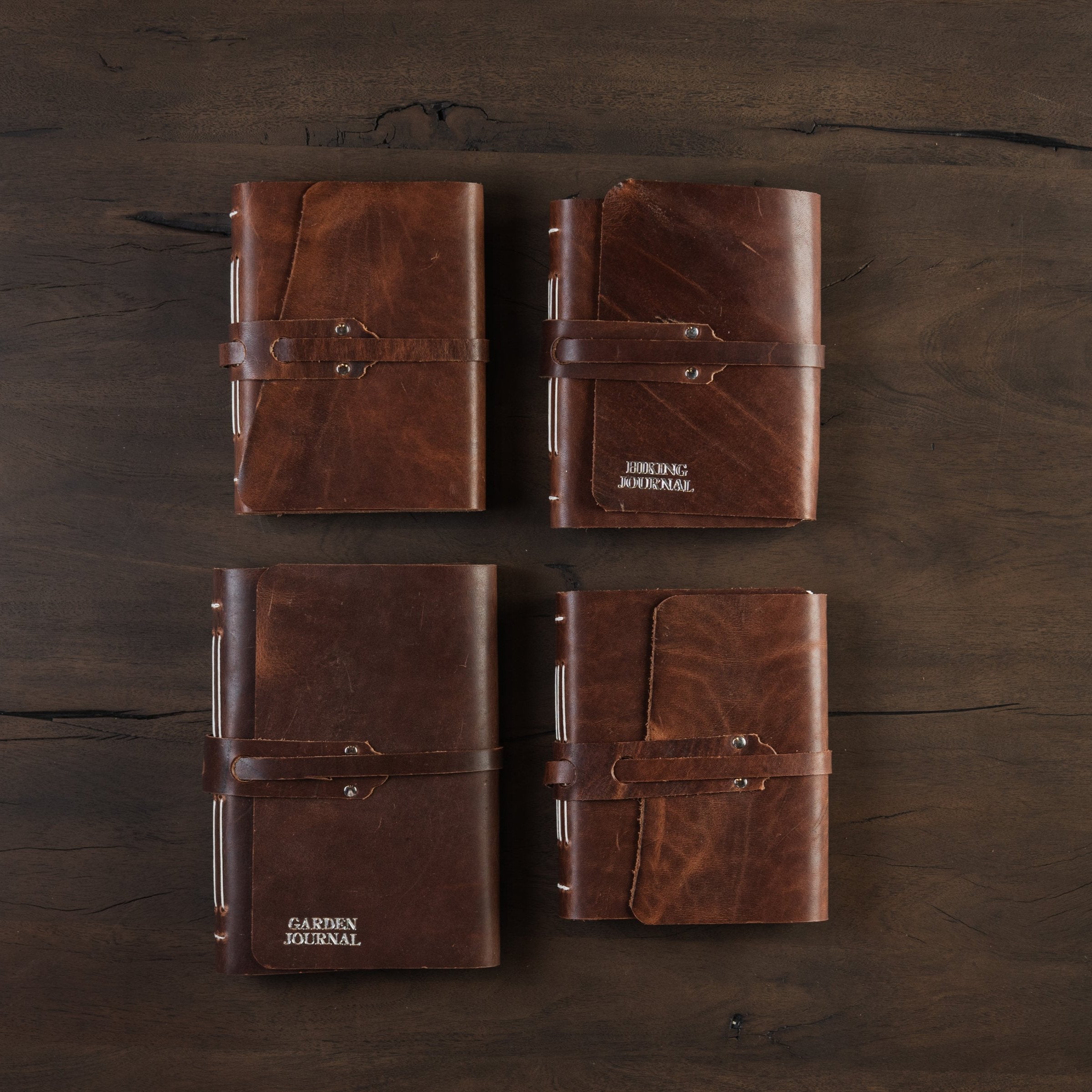 Four leather bound handmade made in Vermont journals on a dark wood table at Addison West