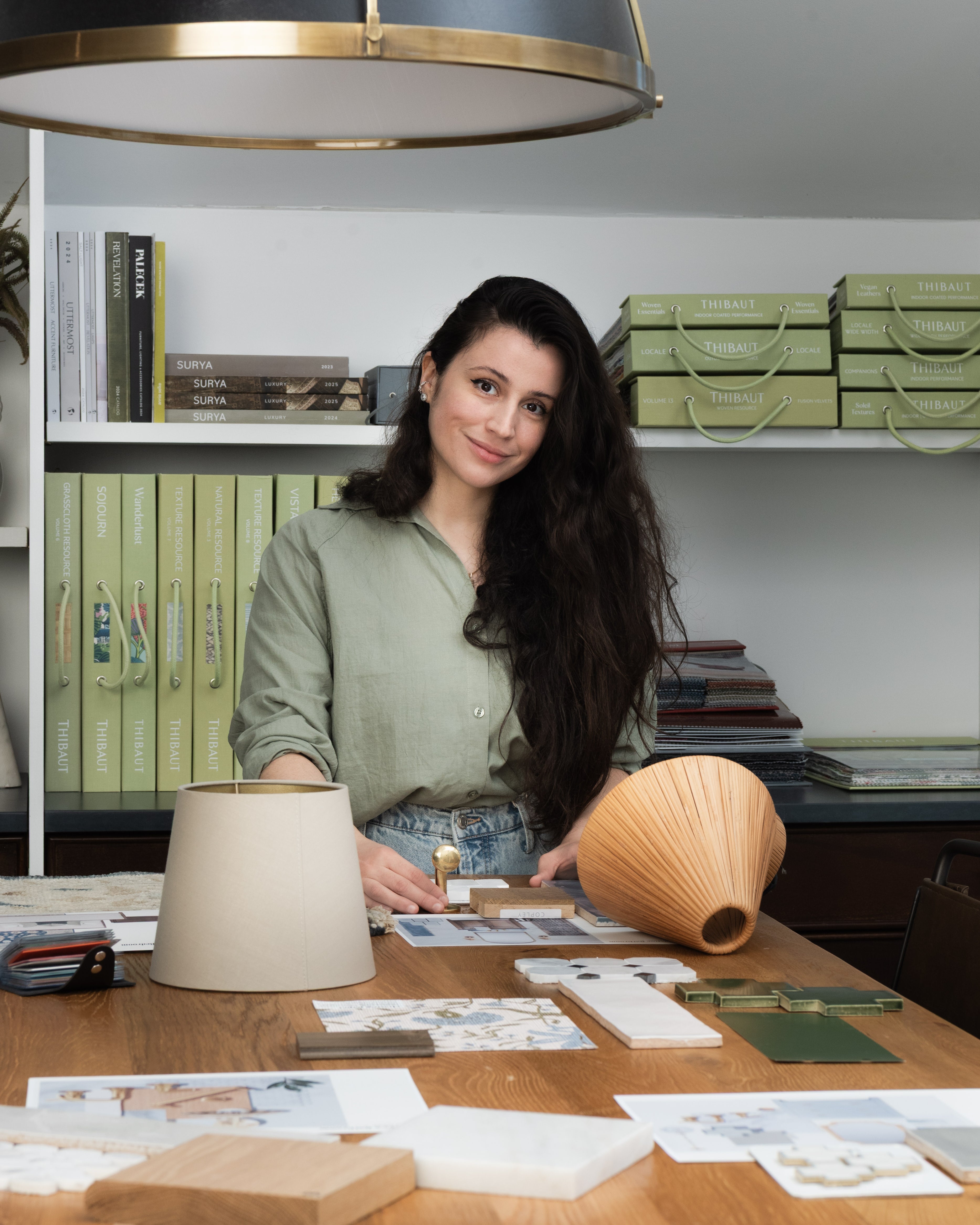 A woman standing at a desk smiling at the camera with interior design samples around her.