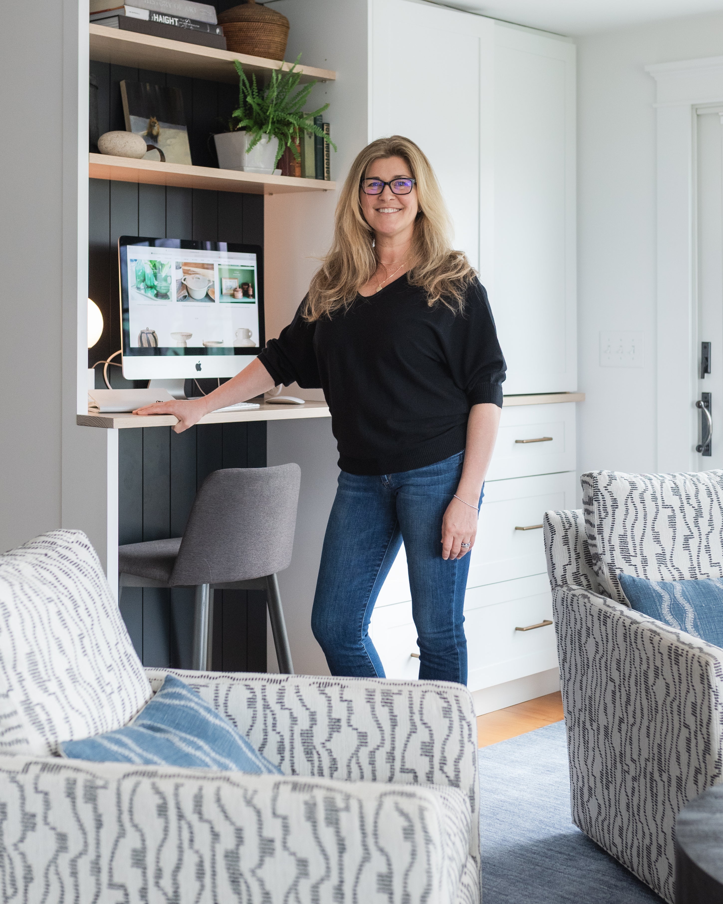 Woman standing in a modern living room with a desk and computer.