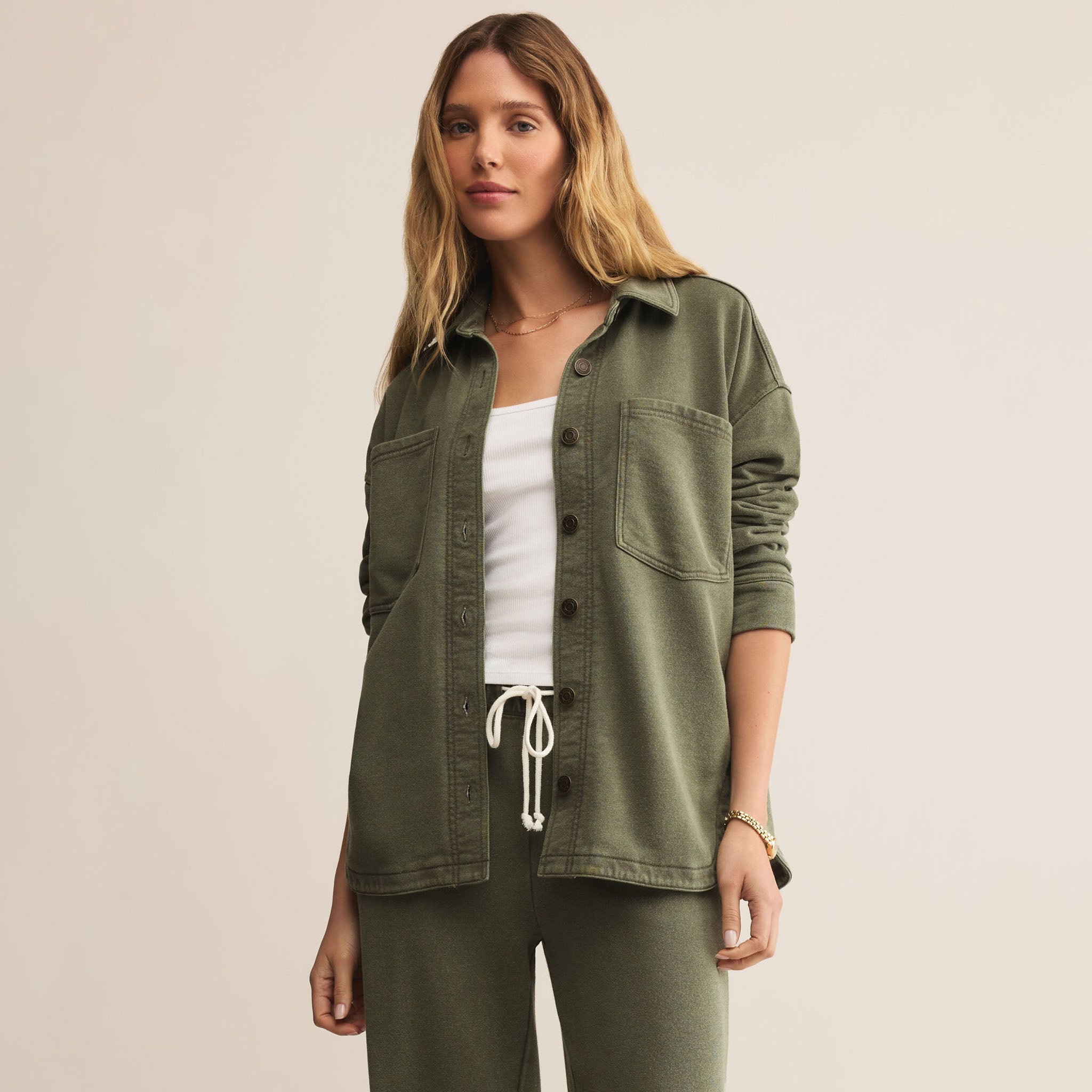 Woman wearing Z supply all day knit olive green jacket and pants on a beige background