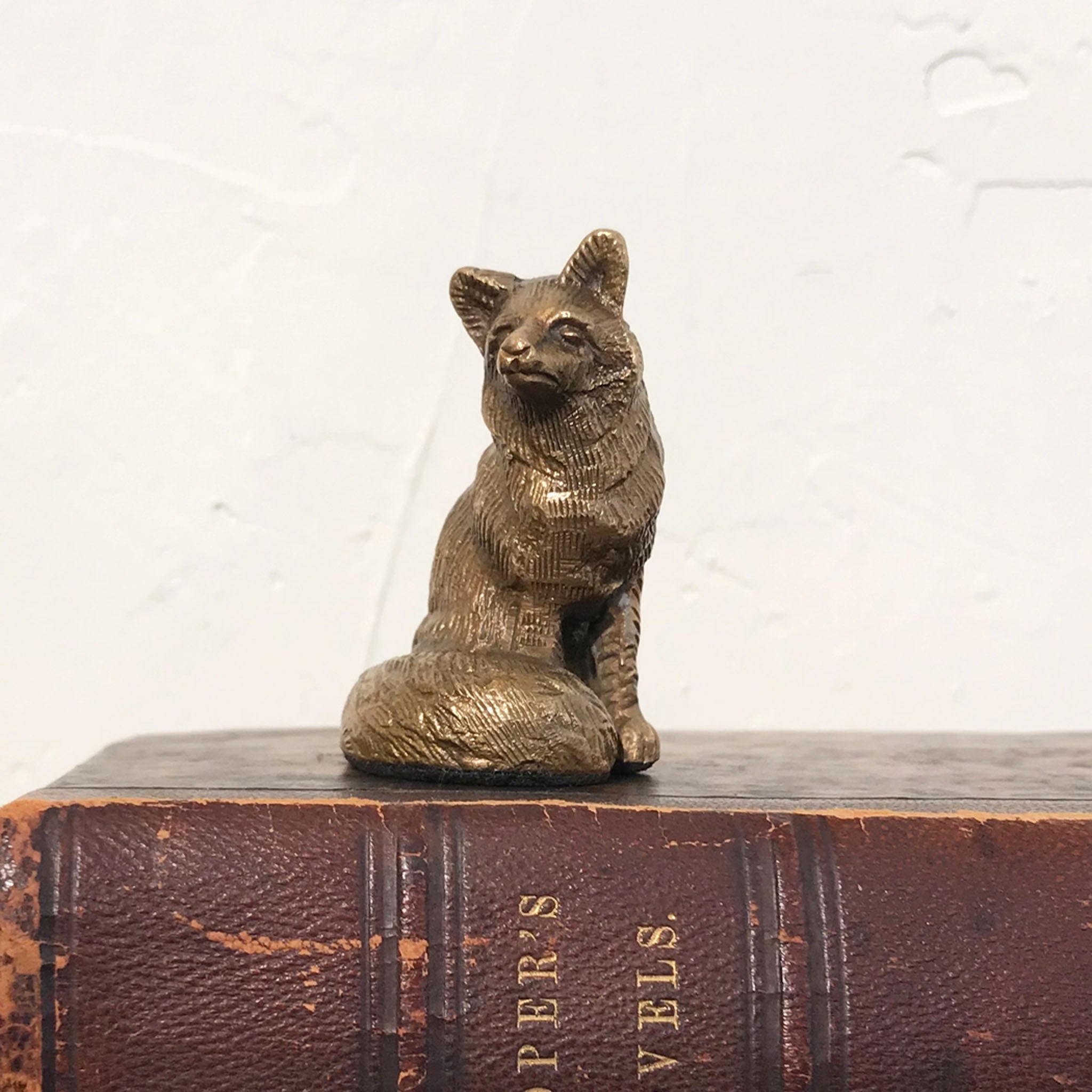Antiqued Brass Sitting Fox figurine on an antique book in front of a white back drop