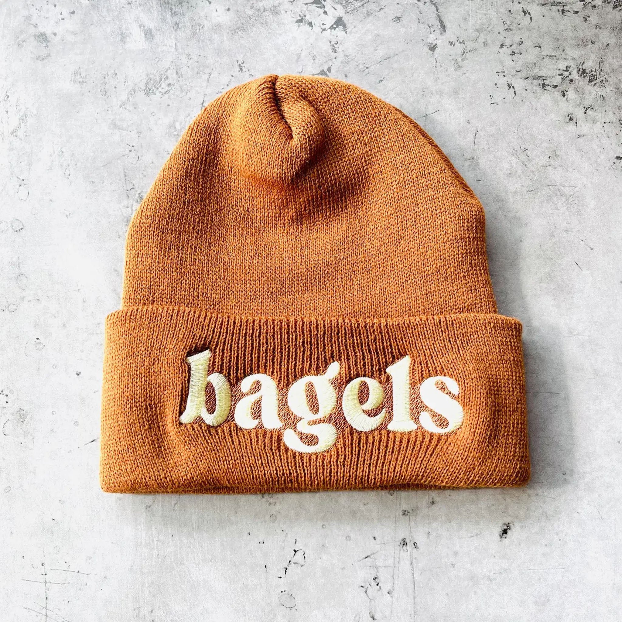 Brown beanie with 'bagels' embroidery on a gray surface
