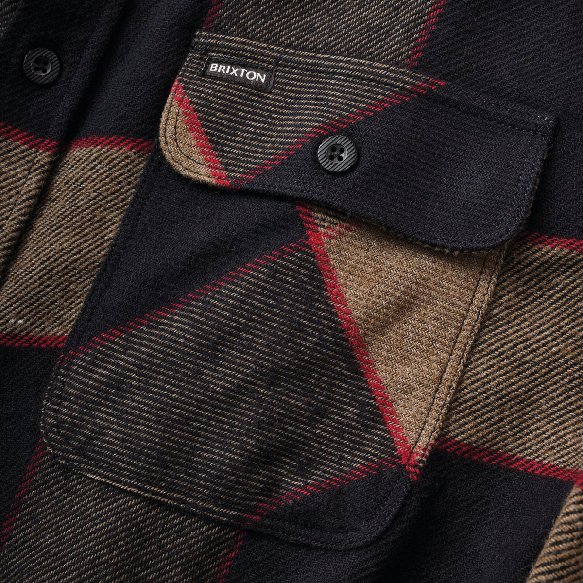 Close up of button up flannel shirt with black, red, grey, and beige plaid and grey buttons.