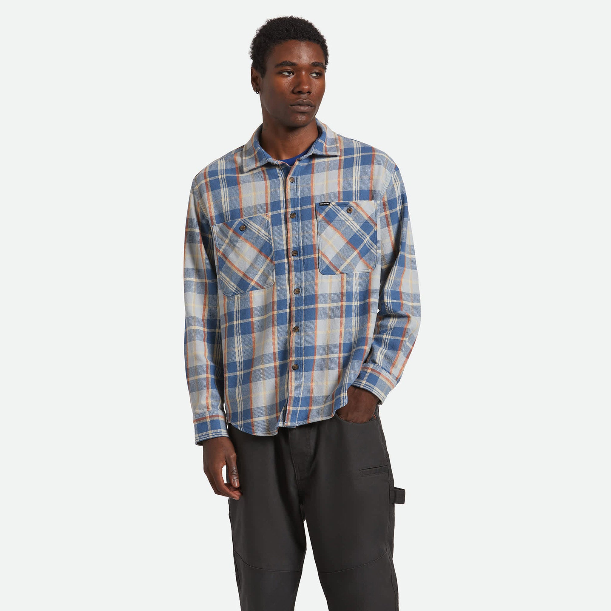 Man wearing a plaid shirt and dark pants on a white background