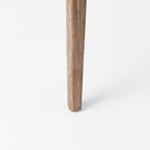 Close up of leg of Clara Light Brown Wood W/ Cream Fabric Seat and Cane Back Armless Dining Chair on a white background