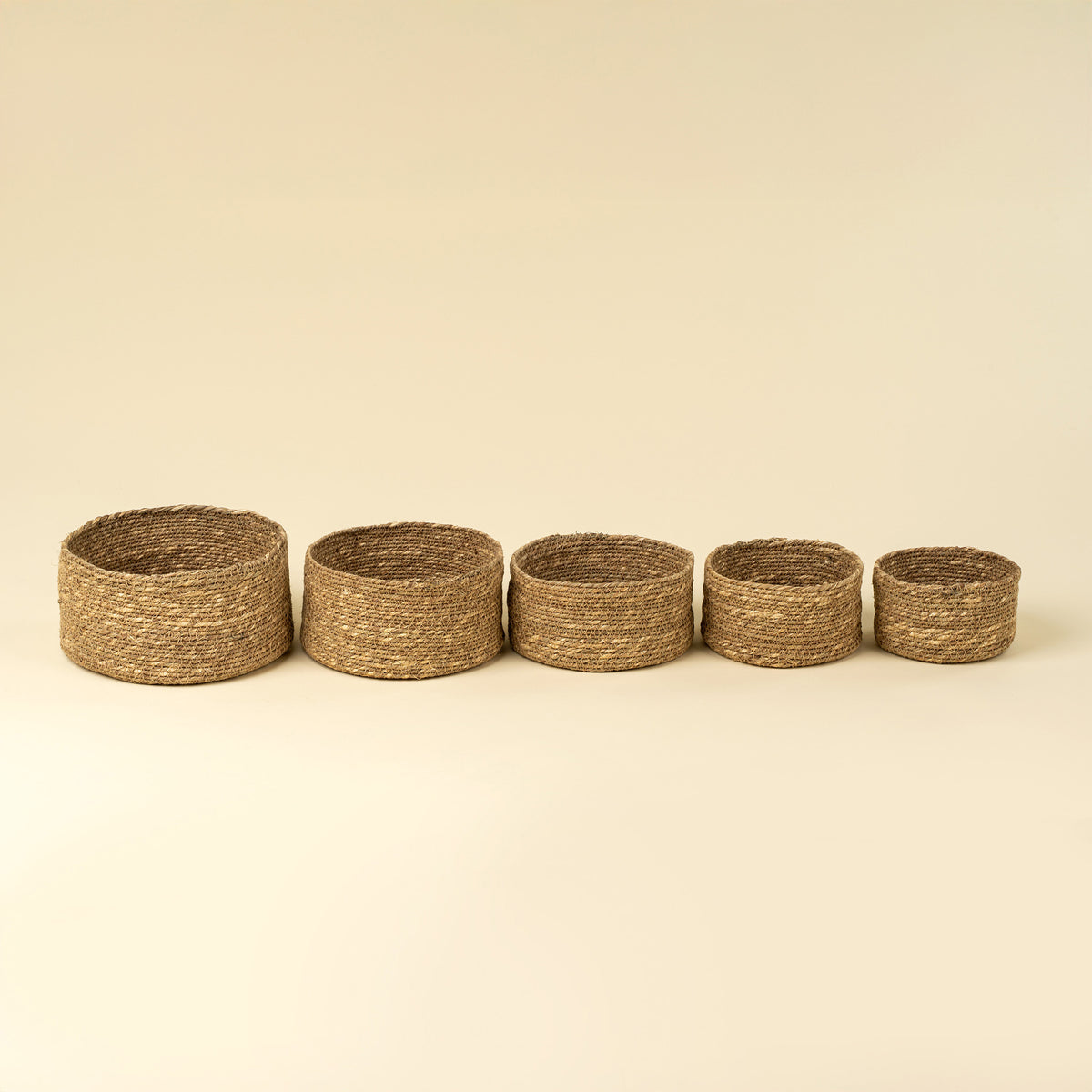 Five woven baskets of varying sizes on a beige background