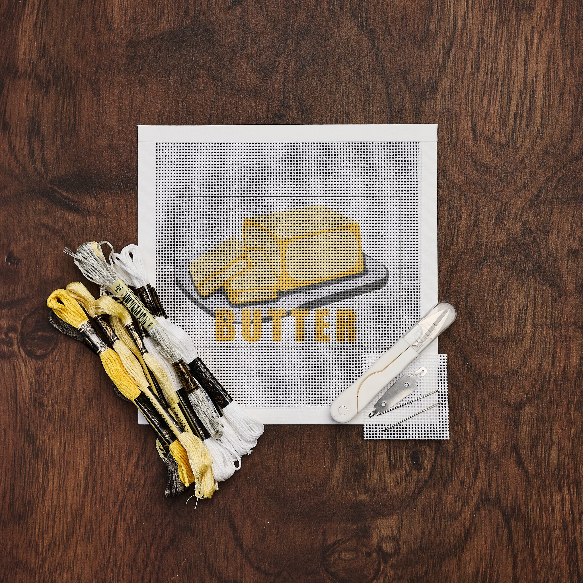 Butter Needlepoint Kit on a wood table at Addison West