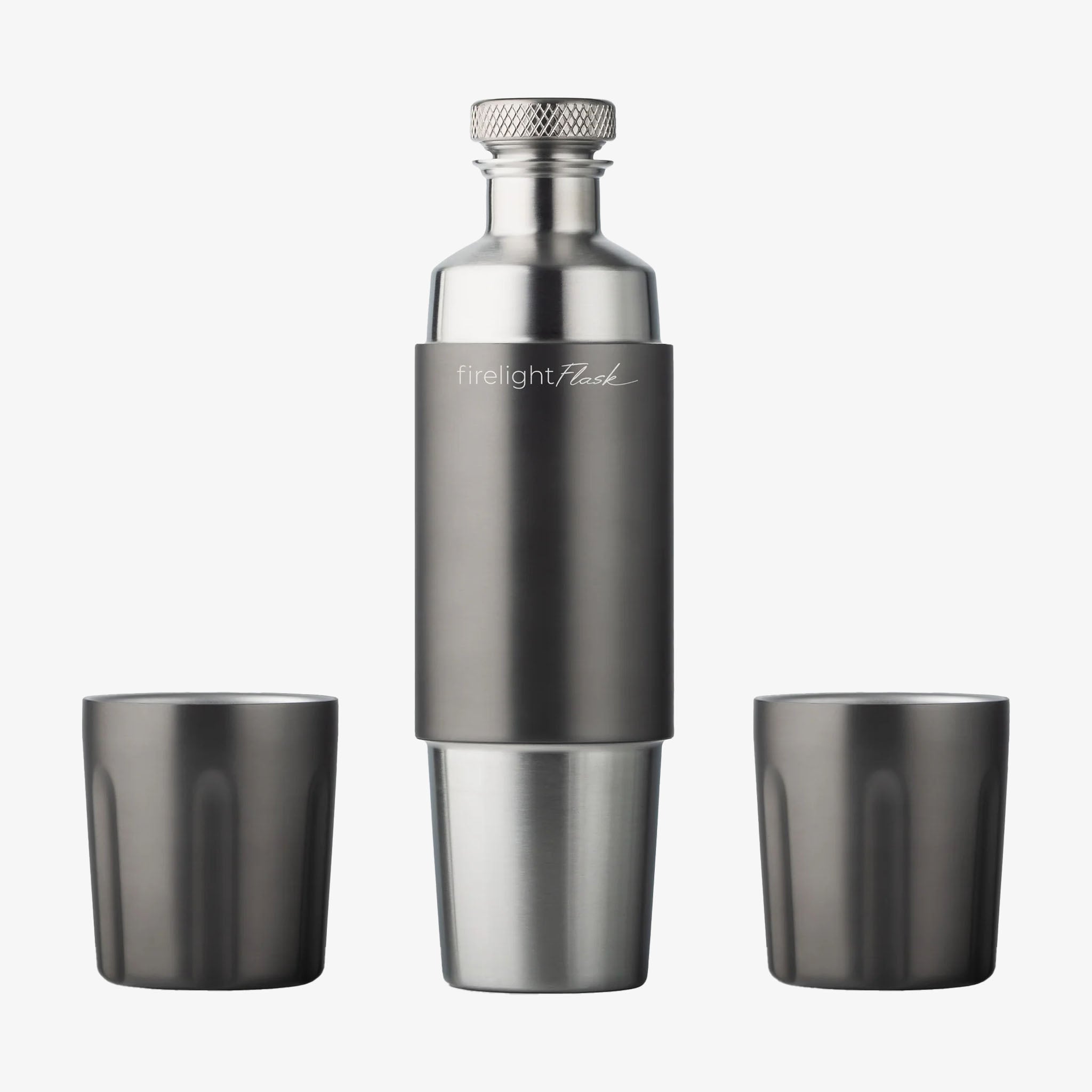 High Camp Flasks gunmetal-colored stainless steel flask with a diamond-patterned cap, accompanied by two matching tumblers, against a white background.