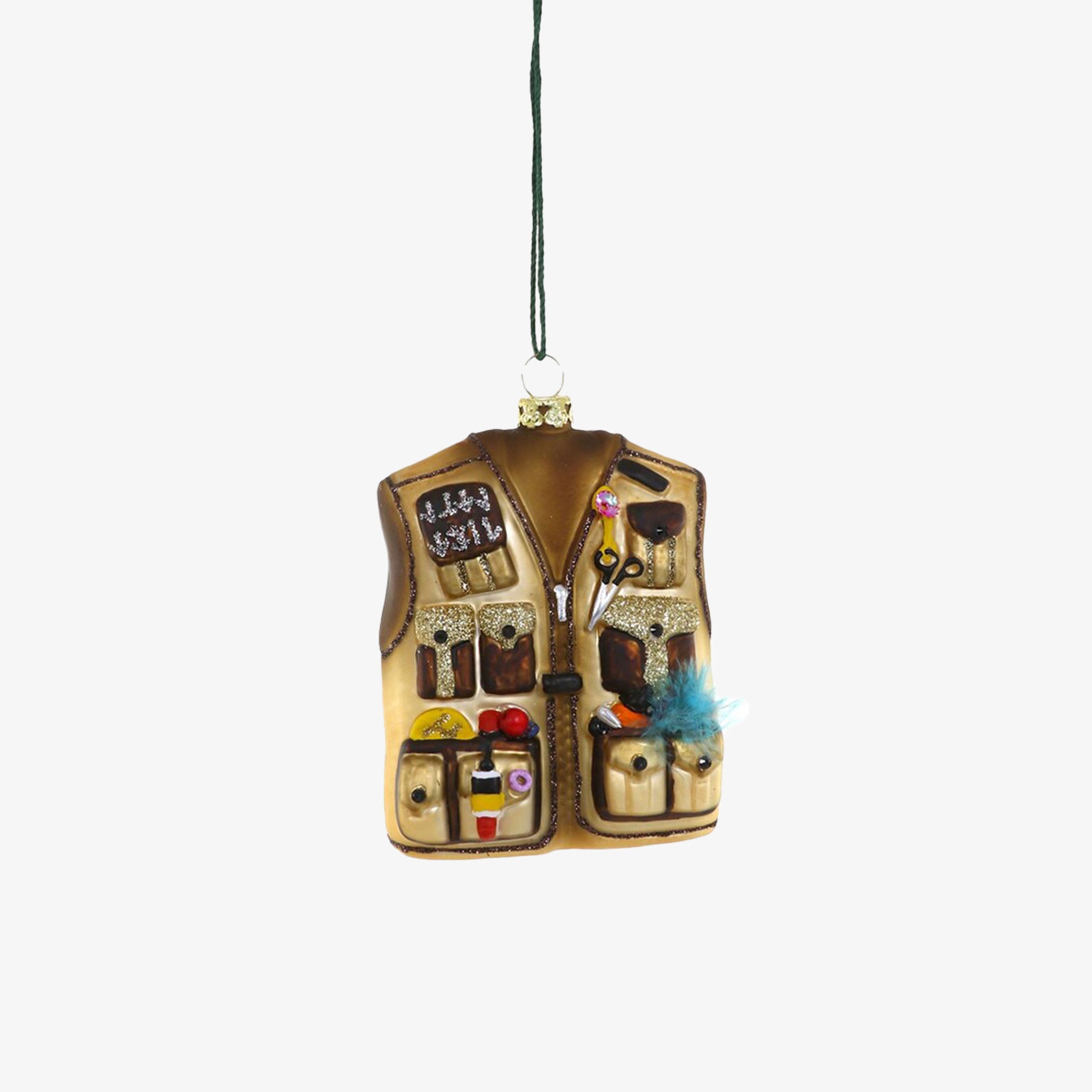 A decorative holiday ornament designed to look like a fly fisherman's vest with various fishing gear attached to it.