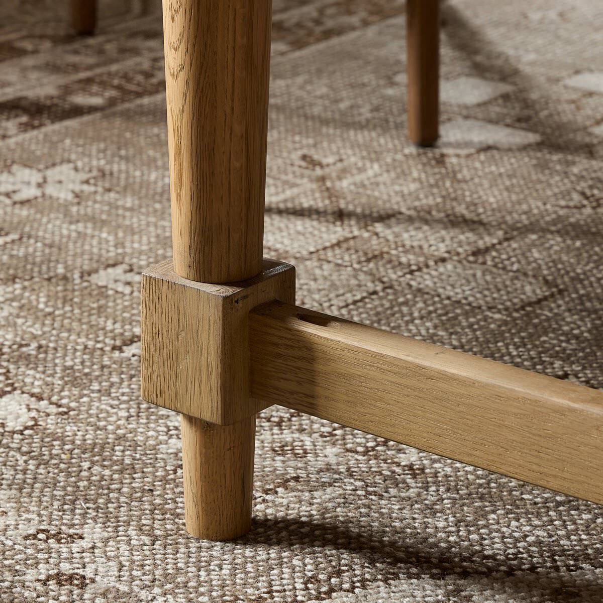Close up of Four Hands Blinn Oval Leaf Extension Dining Table 88"-127" in Worn Oak Veneer on a rug at Addison West