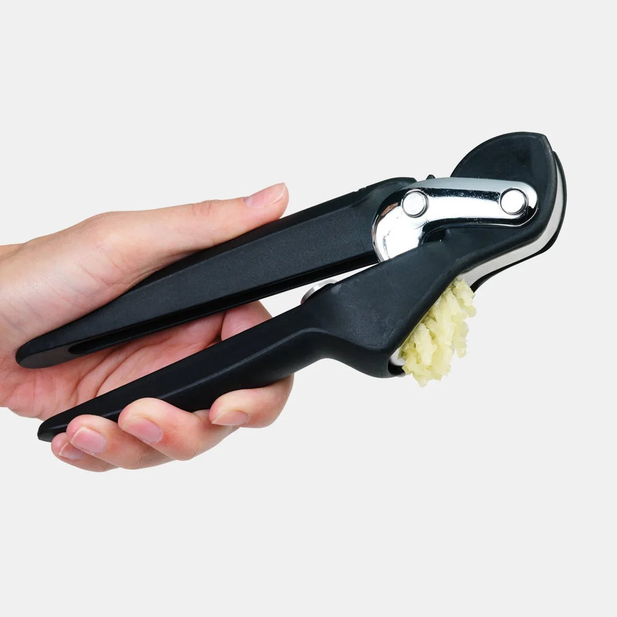 Hand holding a black Chef'n garlic press with minced garlic on a white background