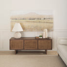 Grier Medium Brown Solid Wood with Cane Media Console in a living room with a painting above it
