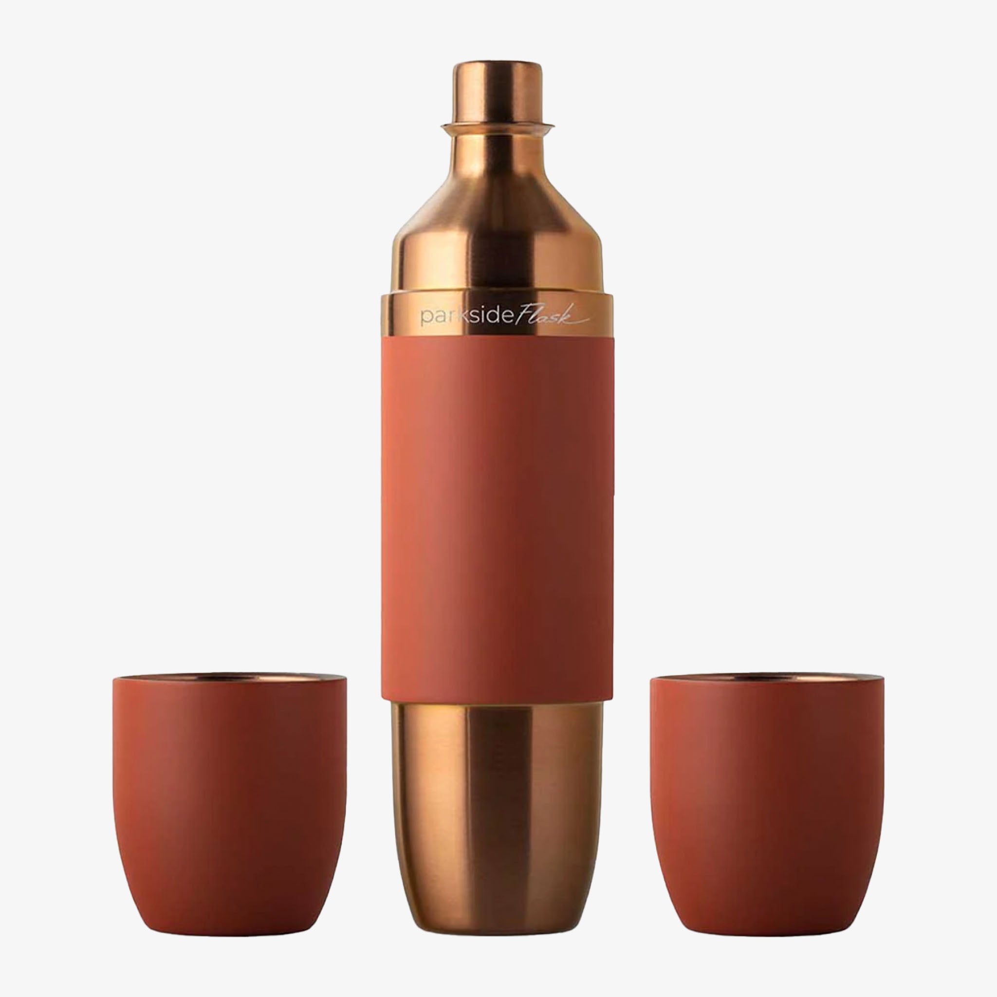 Copper and terracotta-colored flask shaker set with two matching cups on a white background.
