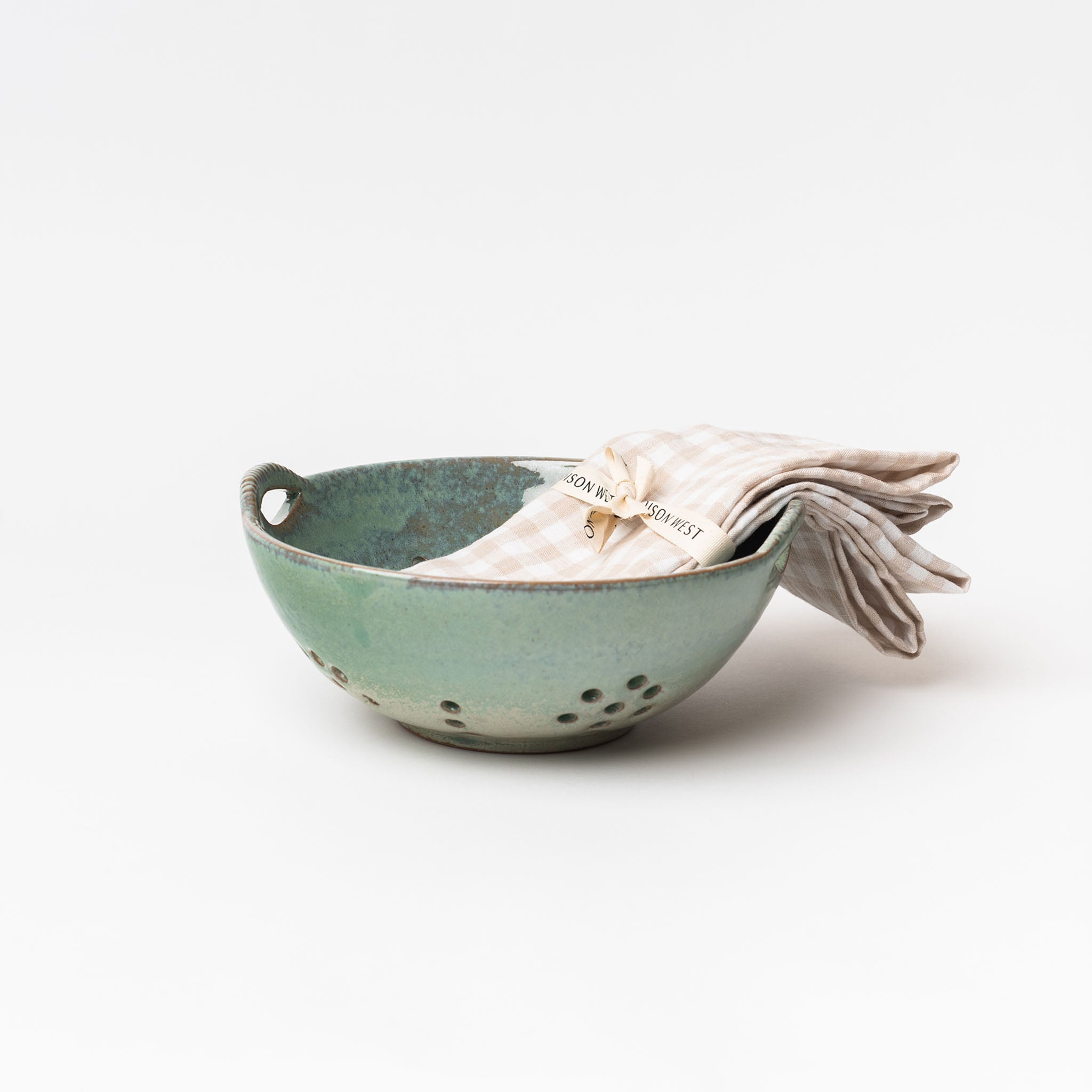 Blue Green glazed berry bowl with plaid napkin on a white background