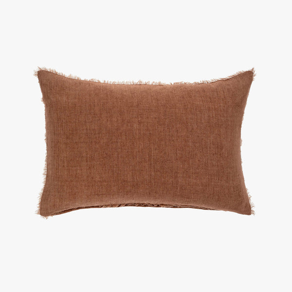 Linen lumbar pillow with frayed edges in burnt red on a white background