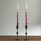Two candle holders made from branches with black bases on a wooden surface.