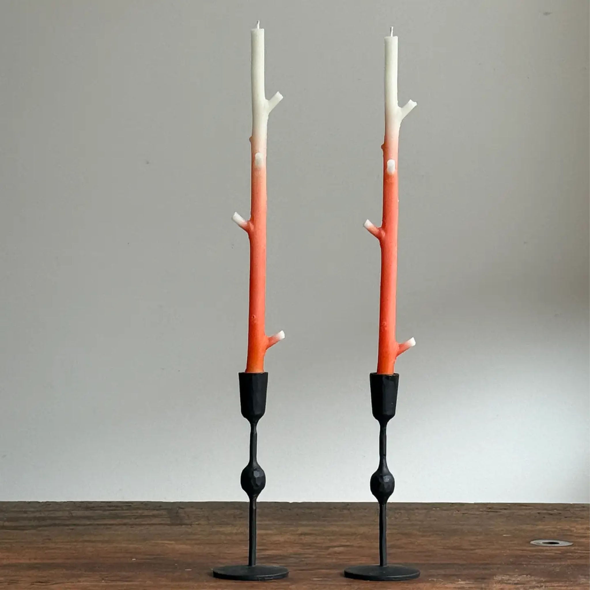 Two candle holders with orange candle holders and black bases on a wooden surface.