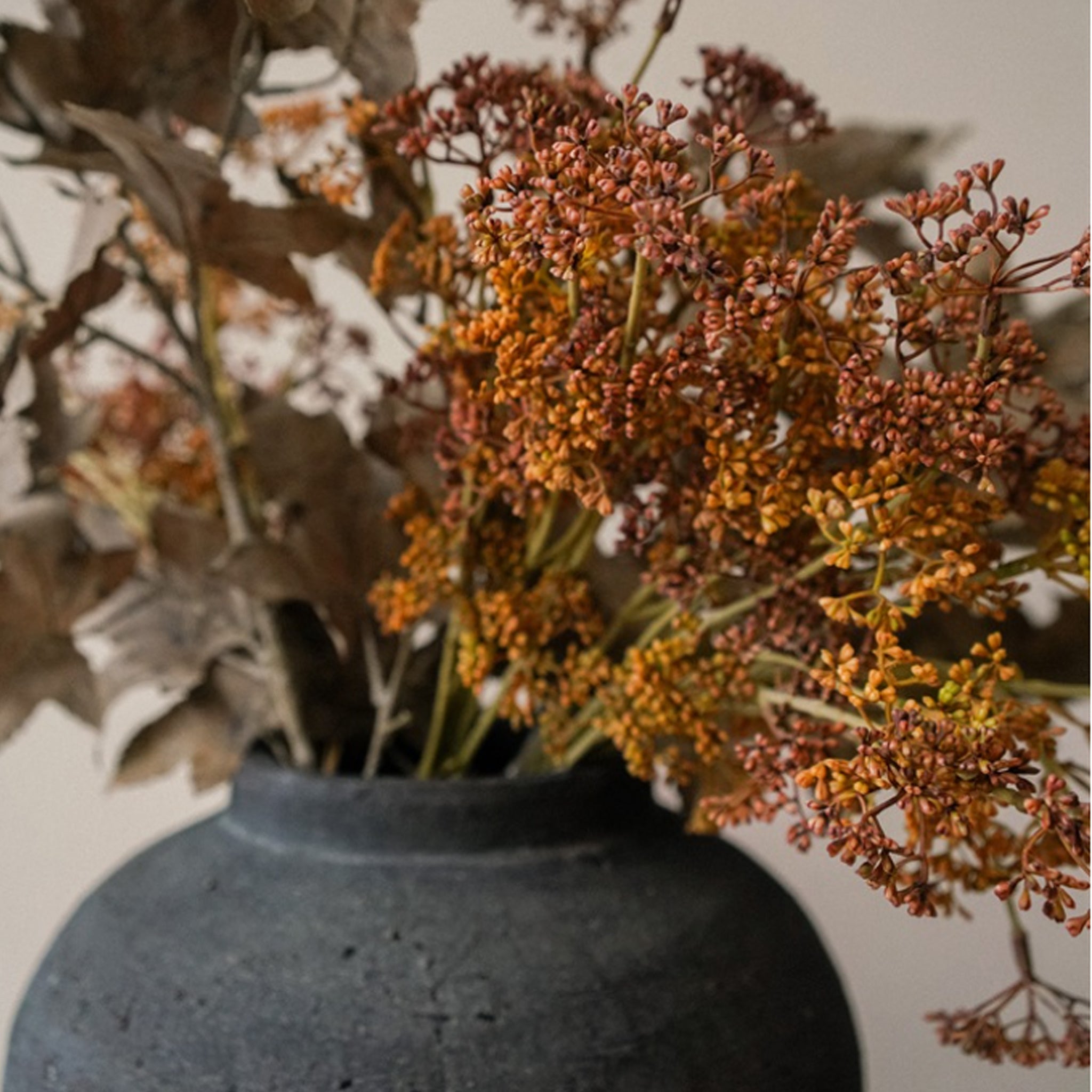 A bouquet of russet-colored artificial meadow grass in a dark ceramic vase.