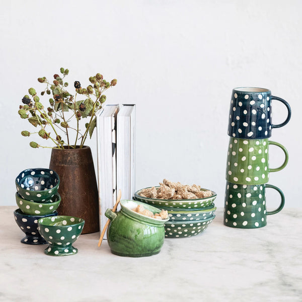 Polkadot Stoneware Mugs in greens and blue stacked on table with bowls and a vase with flowers