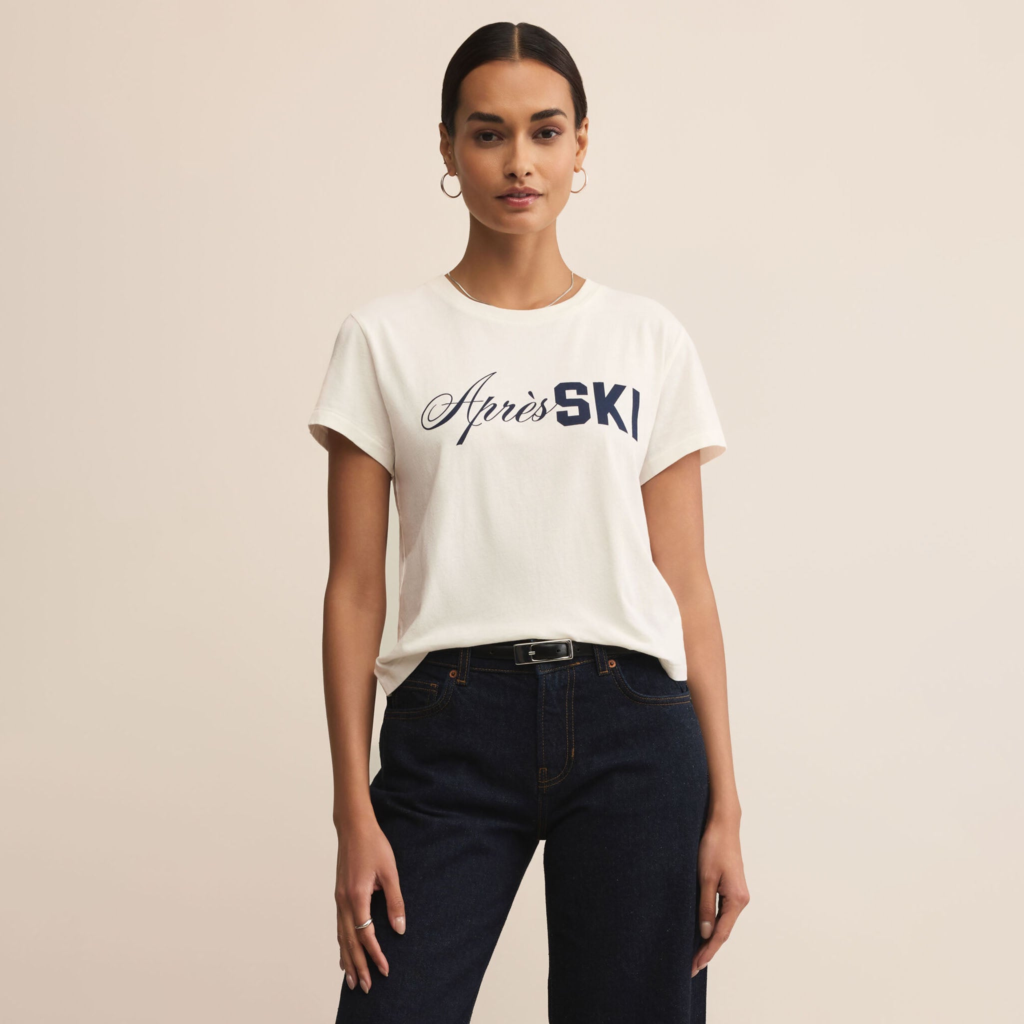 Person wearing a white t-shirt with 'Apres Ski' text on a beige background