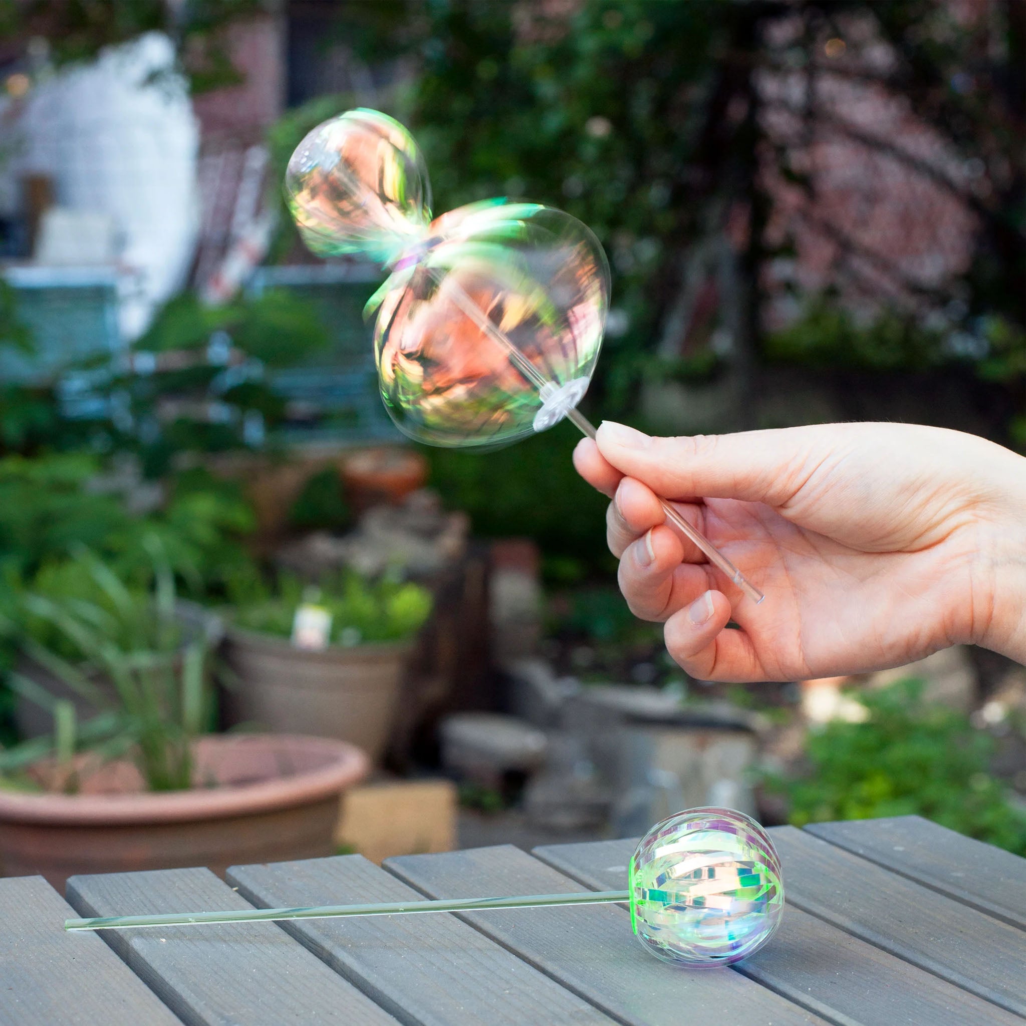 Hand holding Kikkerland rainbow twirler with green plants in the background