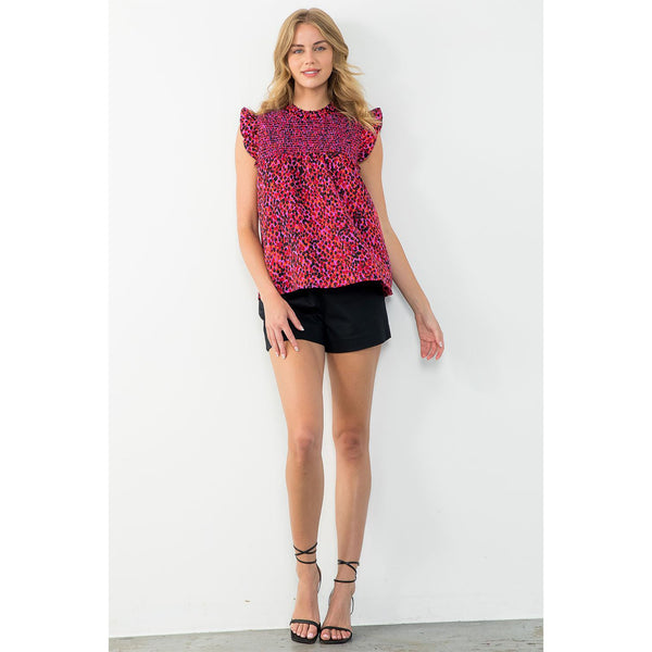 Blond model wearing THML Ruffle Sleeve Smocked Top in fuschia and purple in front of a white wall