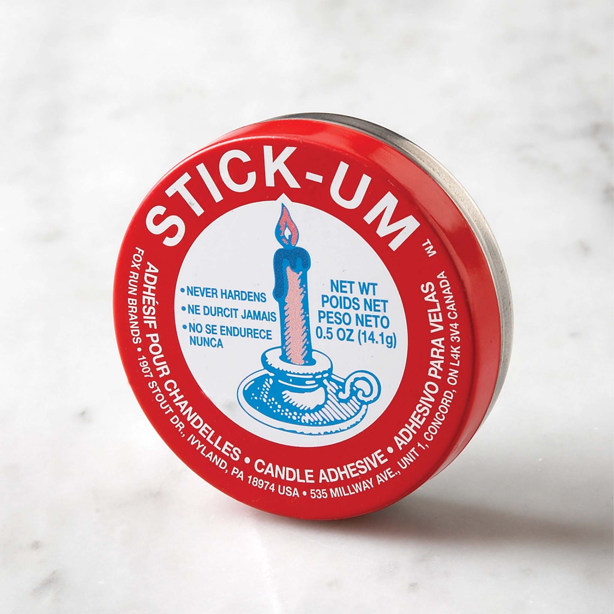 A red container of Stick-Um candle adhesive with a white and blue label, on a marble surface.