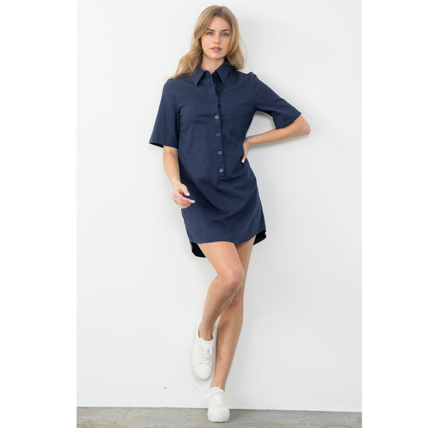Model wearing THML Short Sleeve Button Up Dress in Navy with sneakers in front of a neutral wall 