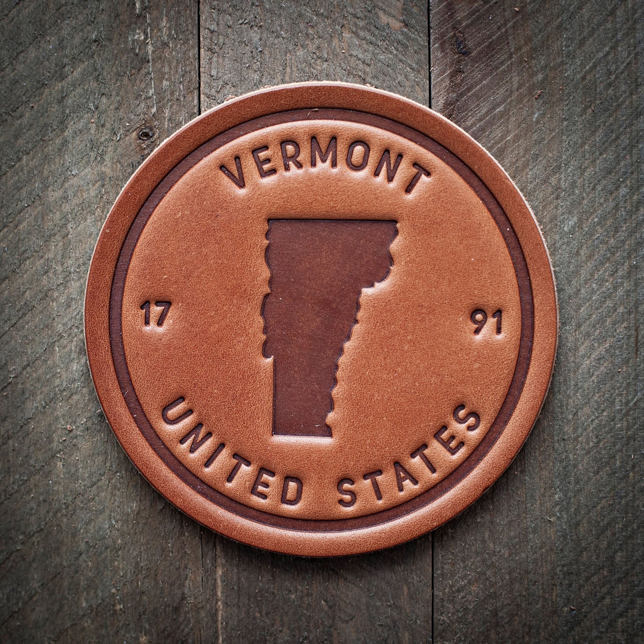 A brown leather coaster with the embossed text 'Vermont United States 1791' on a wooden surface.
