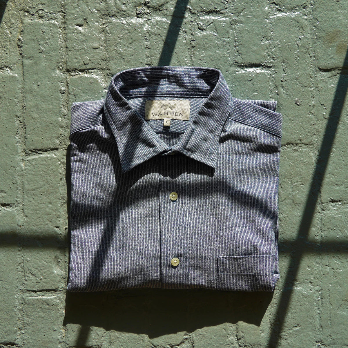 Warren Windsor Button Down in Blue Stripe on a brick wall at Addison West