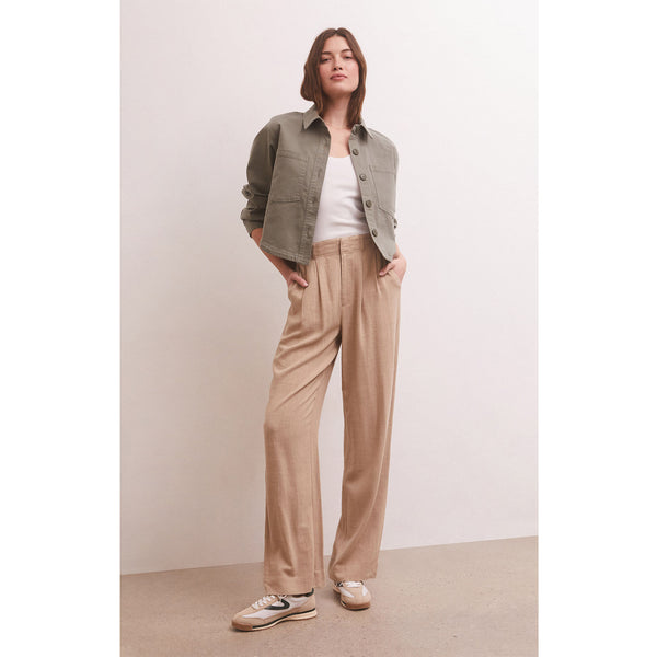 Model wearing Z supply Z Supply All Day Cropped Twill Jacket in Evergreen with loose khaki pants and sneakers in front of a beige wall