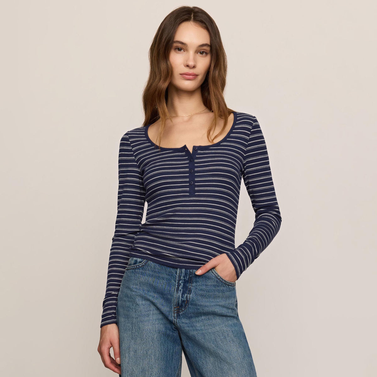 Woman wearing a blue and white striped long-sleeve top and jeans on a beige background