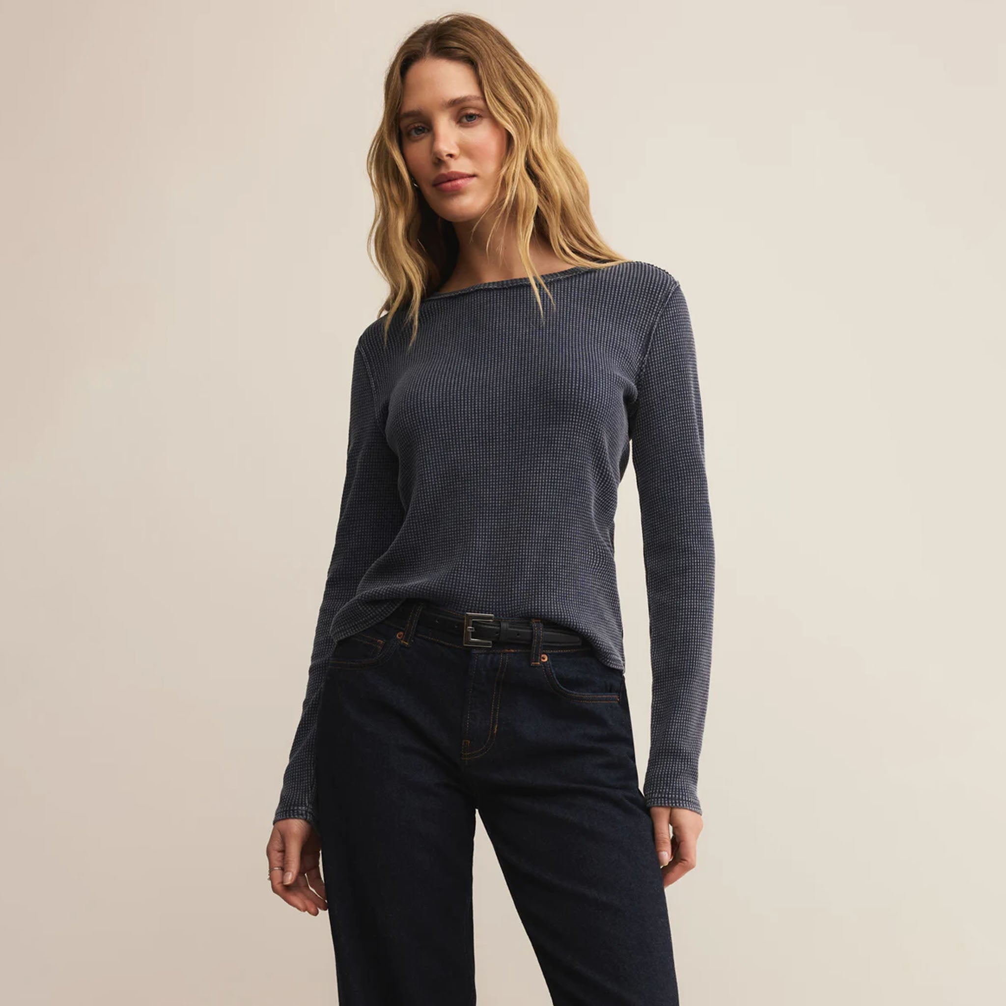 Woman wearing a dark blue long-sleeve top and black pants on a beige background