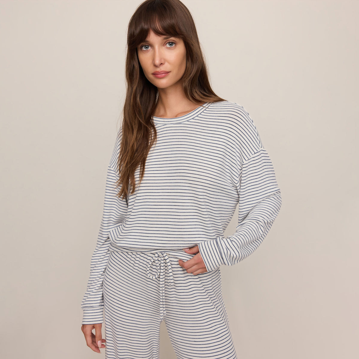 Woman wearing a striped long-sleeve top and pants on a beige background