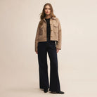 Woman wearing a beige jacket and black pants on a beige background