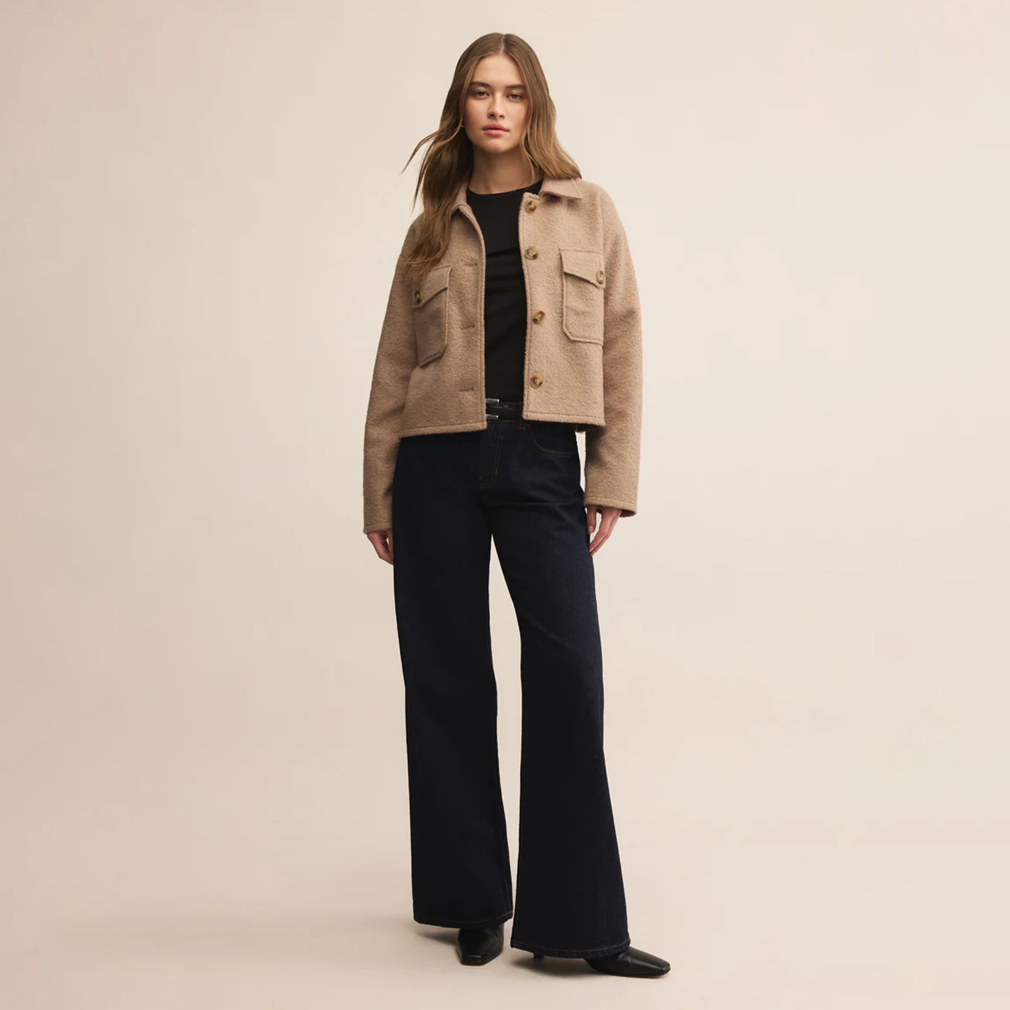 Woman wearing a beige jacket and black pants on a beige background