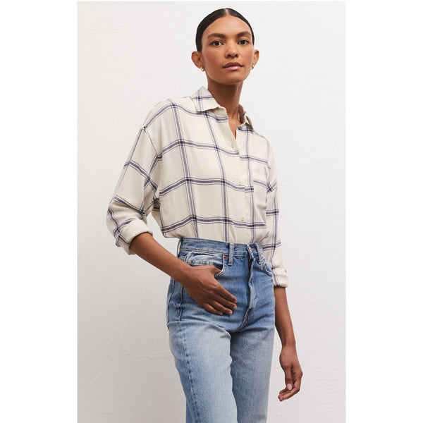 Model wearing jeans and Z Supply River Plaid Button Up in Inca in front of a white wall